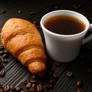 Croissants with coffee and coffee beans on a wooden background.